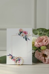 Photo of Blank invitation card, ring, eucalyptus leaves and flowers on white wooden table