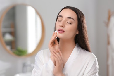 Beautiful woman removing makeup with cotton pad indoors