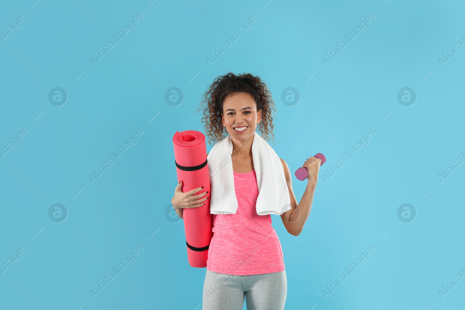 Photo of Beautiful African American woman with yoga mat, towel and dumbbell on turquoise background