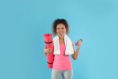 Beautiful African American woman with yoga mat, towel and dumbbell on turquoise background