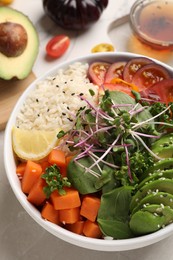 Delicious vegan bowl with avocados, carrots and microgreens on grey table, closeup