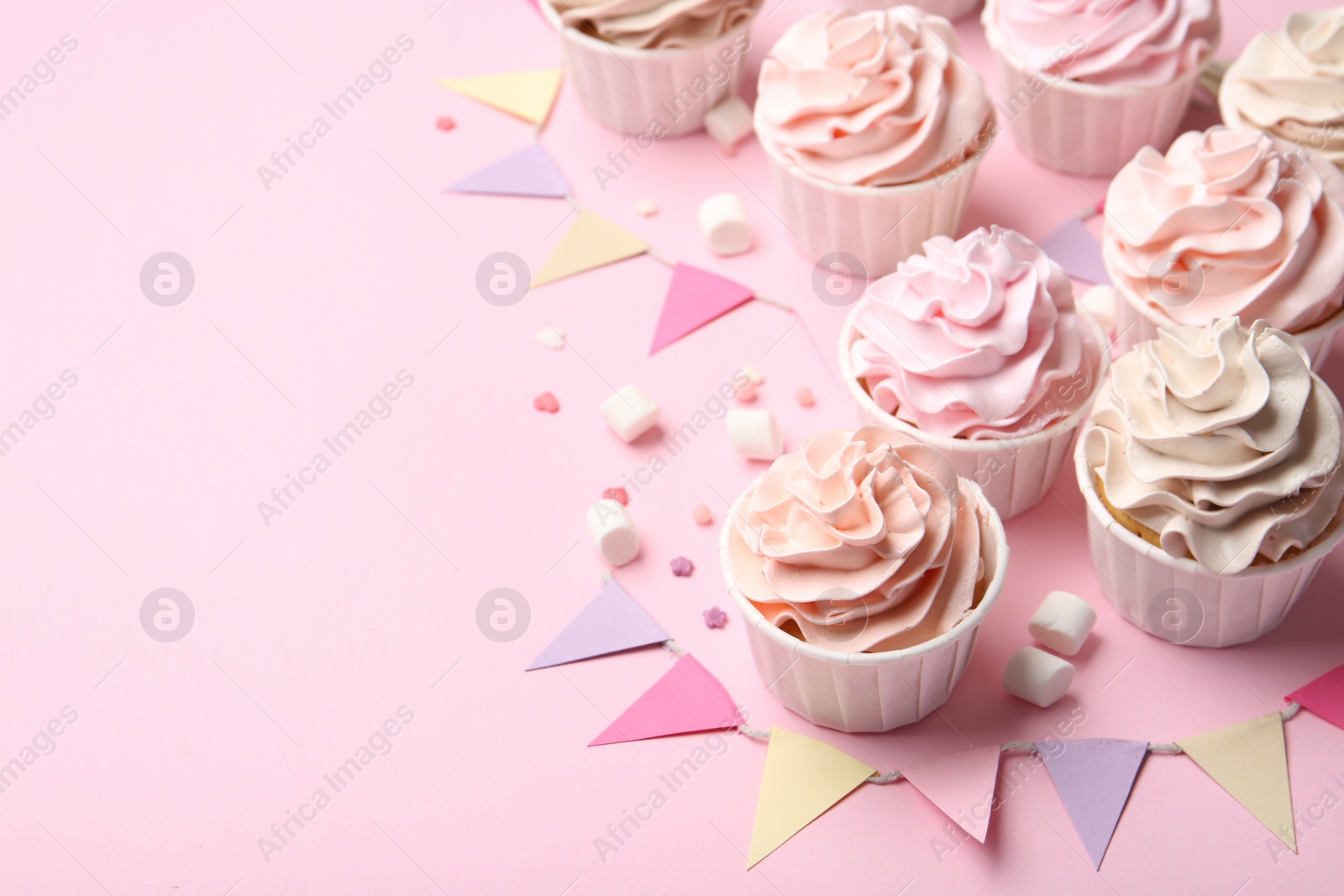 Photo of Delicious birthday cupcakes, bunting flags, marshmallows and sprinkles on pink background. Space for text