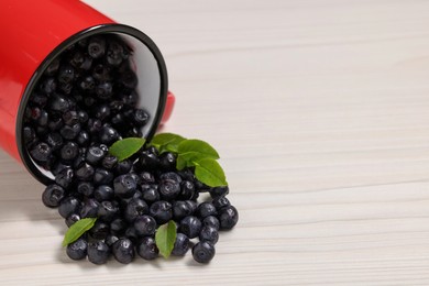 Mug with ripe bilberries on white wooden table, closeup. Space for text