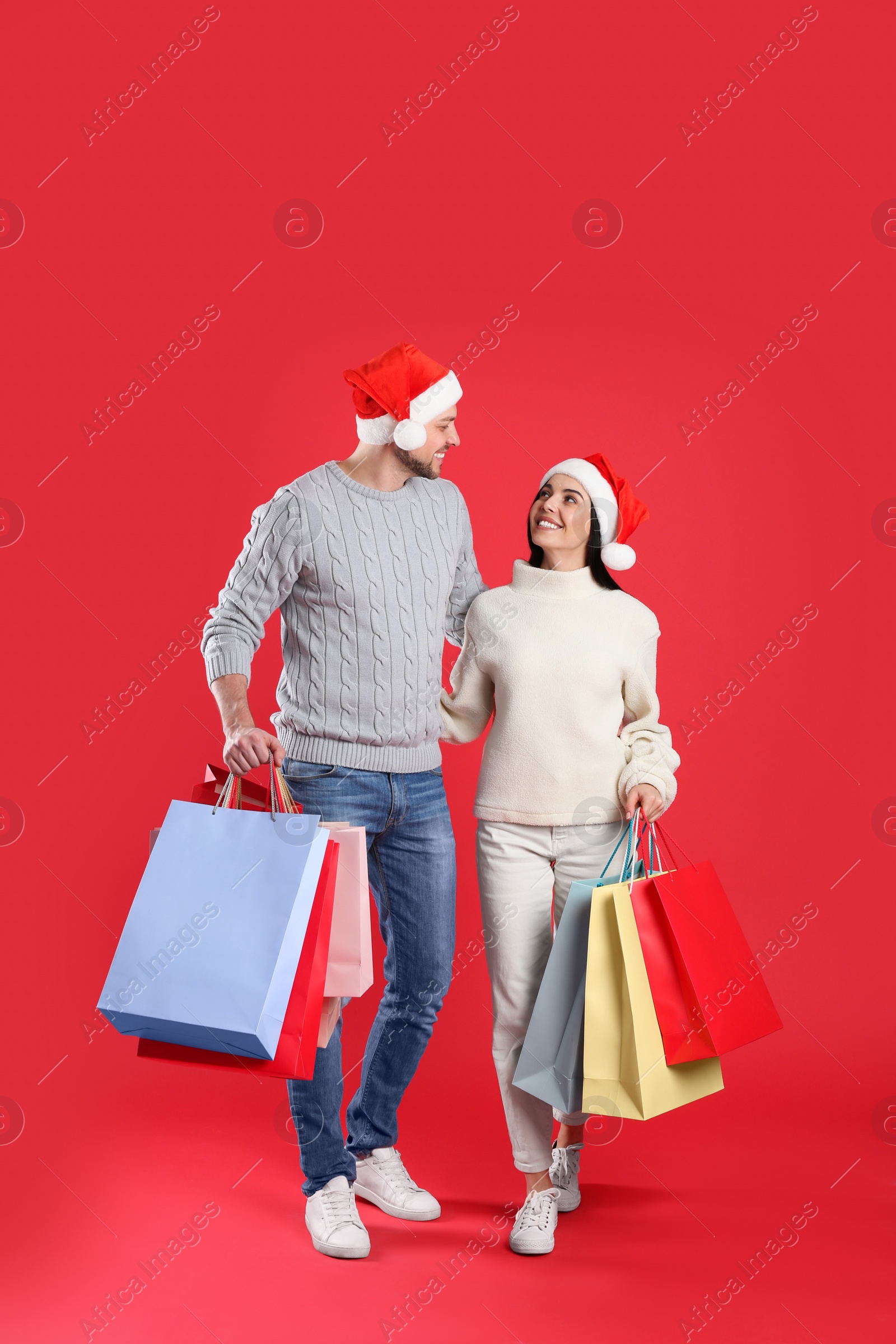 Photo of Happy couple with paper bags on red background. Christmas shopping