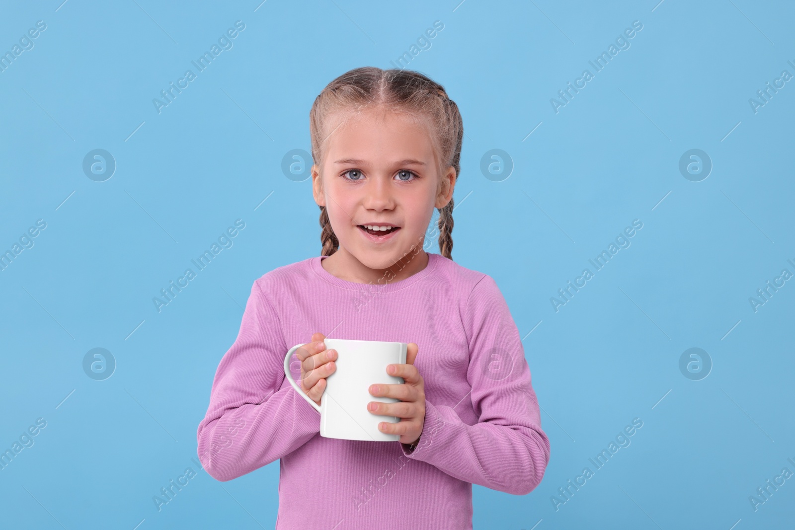 Photo of Happy girl with white ceramic mug on light blue background