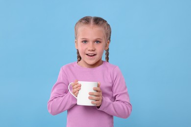 Photo of Happy girl with white ceramic mug on light blue background