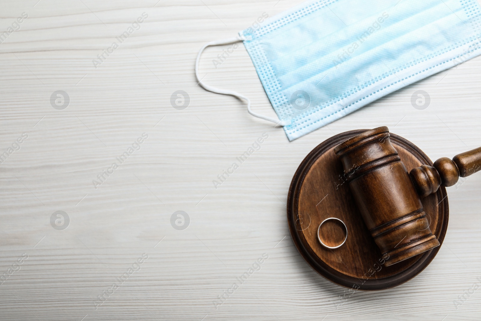 Photo of Gavel, wedding ring and protective mask on white wooden table, flat lay with space for text. Divorce during coronavirus quarantine