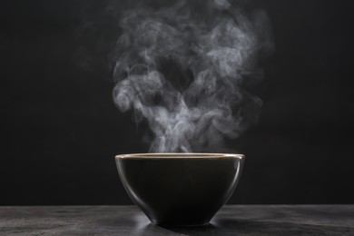 Photo of Steaming ceramic bowl on grey table against dark background