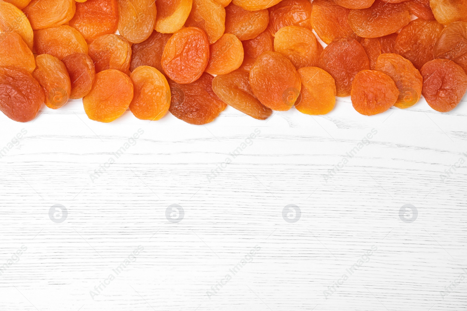 Photo of Dried apricots on white wooden table, top view with space for text. Healthy fruit
