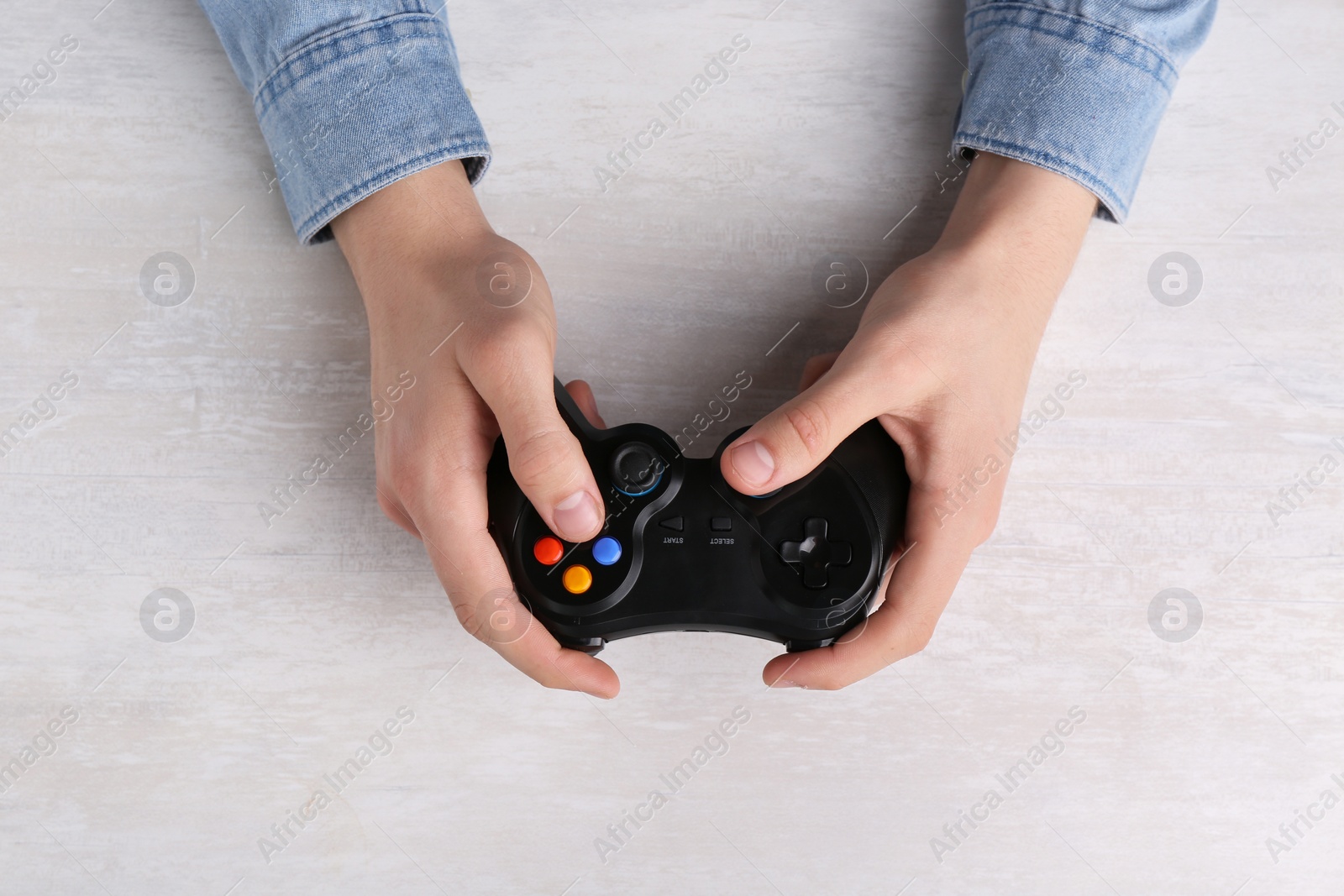 Photo of Man using wireless game controller at white table, top view