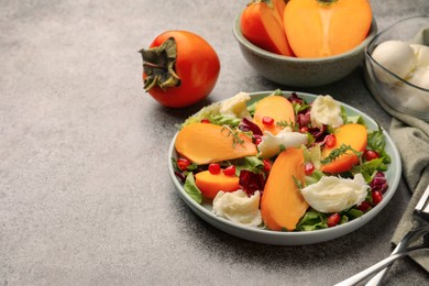 Delicious persimmon salad with cheese and pomegranate served on grey table. Space for text