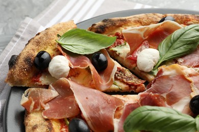 Tasty pizza with cured ham, olives, mozzarella cheese, sun-dried tomato and basil on table, closeup