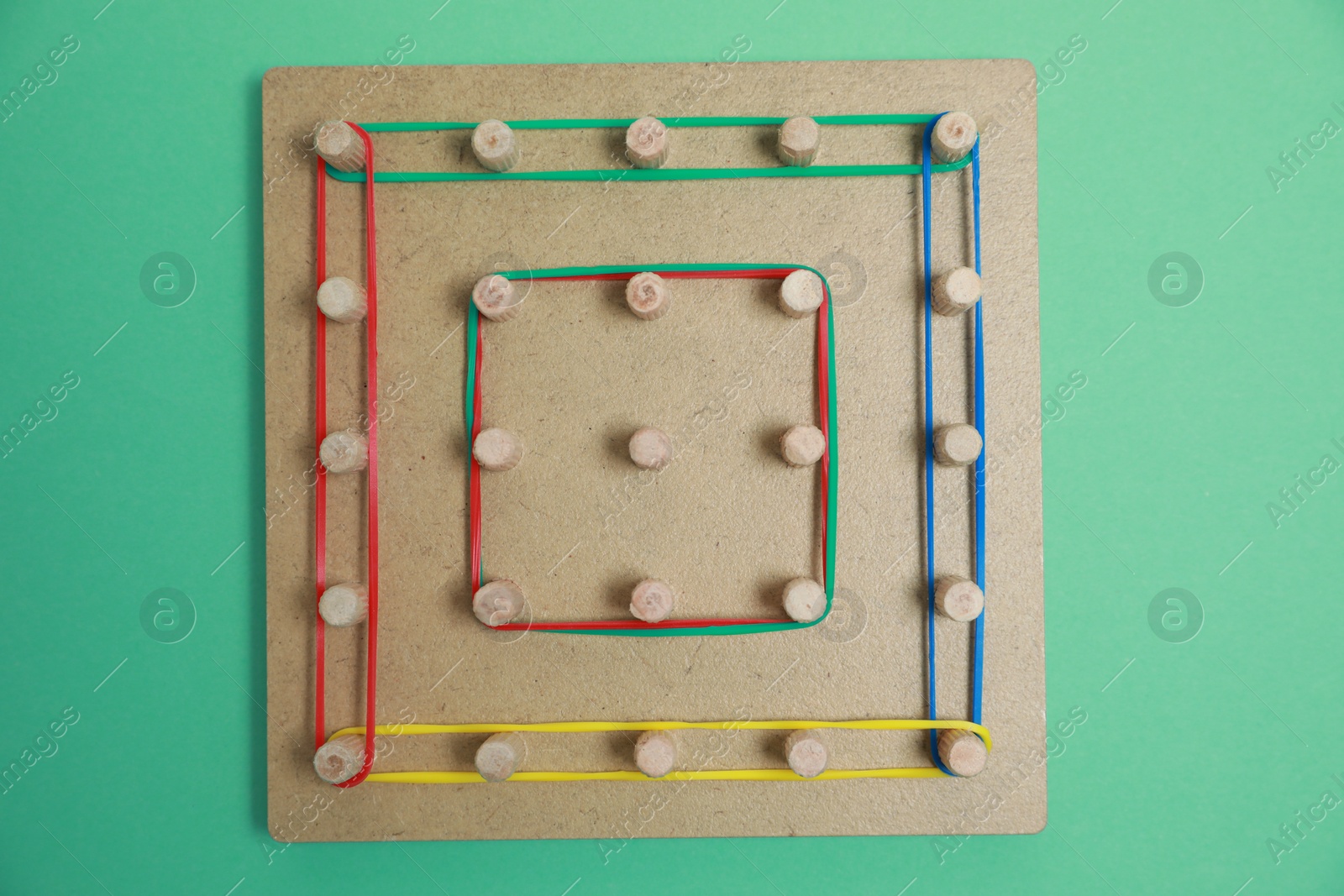 Photo of Wooden geoboard with rubber bands on green background, top view. Educational toy for motor skills development