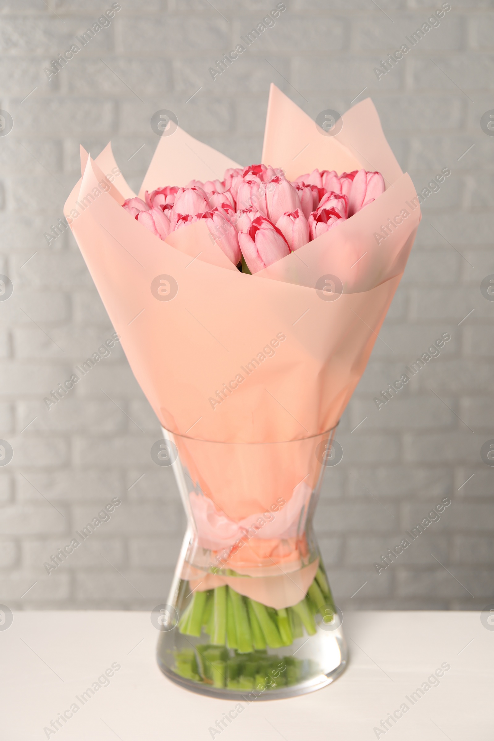 Photo of Bouquet of beautiful pink tulips in vase on white table near brick wall
