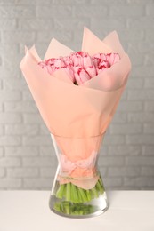 Bouquet of beautiful pink tulips in vase on white table near brick wall