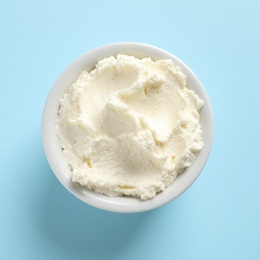 Bowl of tasty cream cheese on color background, top view