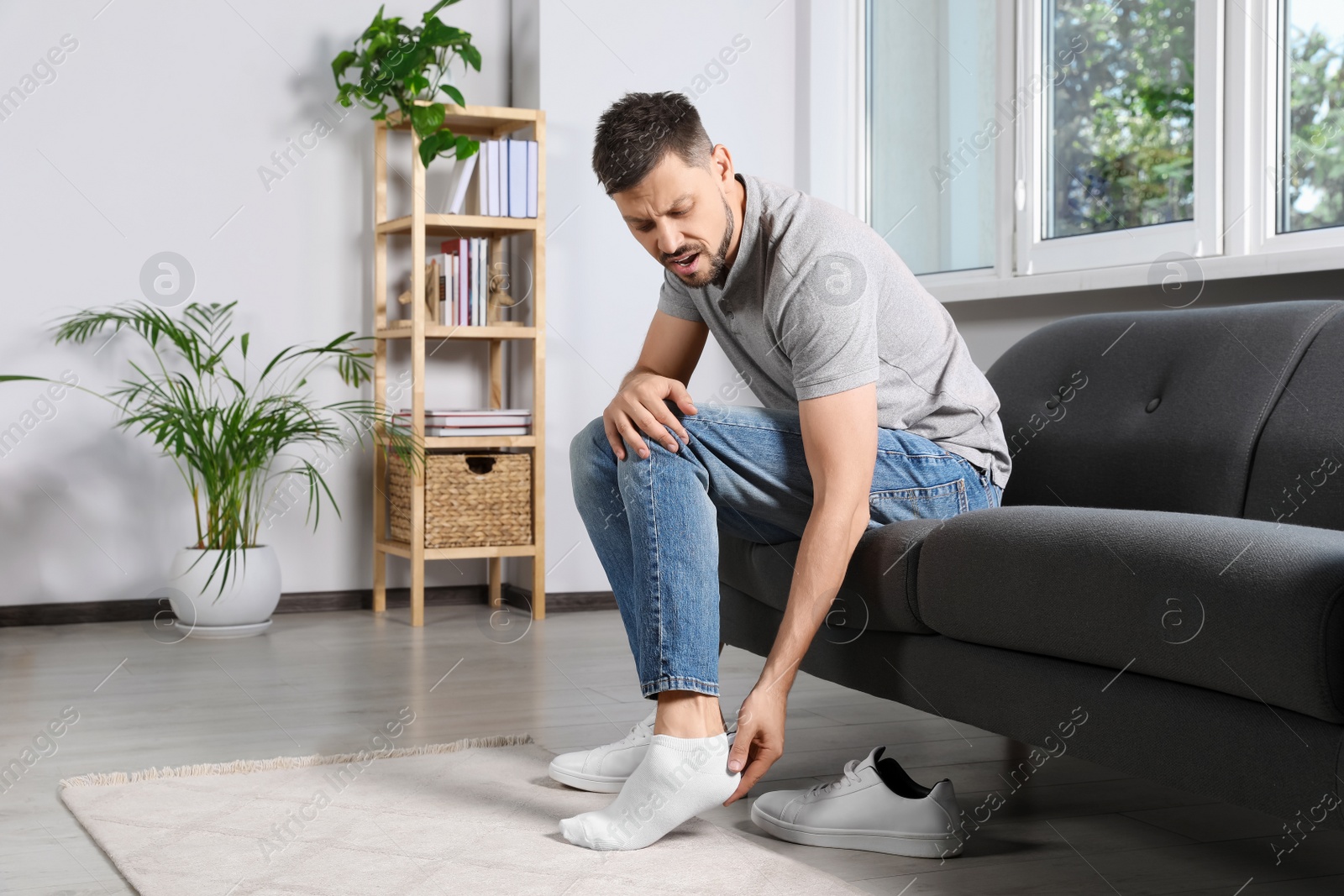 Photo of Man suffering from foot pain at home, space for text