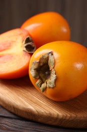 Photo of Whole and cut delicious ripe persimmons on wooden table, closeup