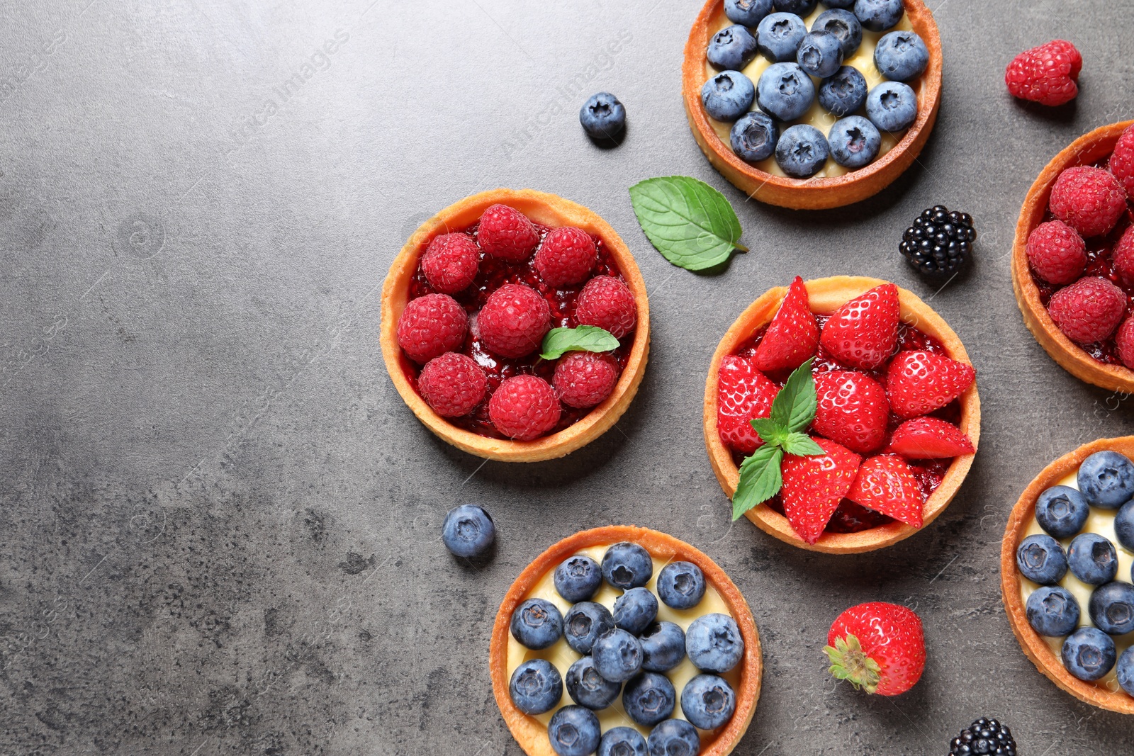 Photo of Tartlets with different fresh berries on grey table, flat lay and space for text. Delicious dessert