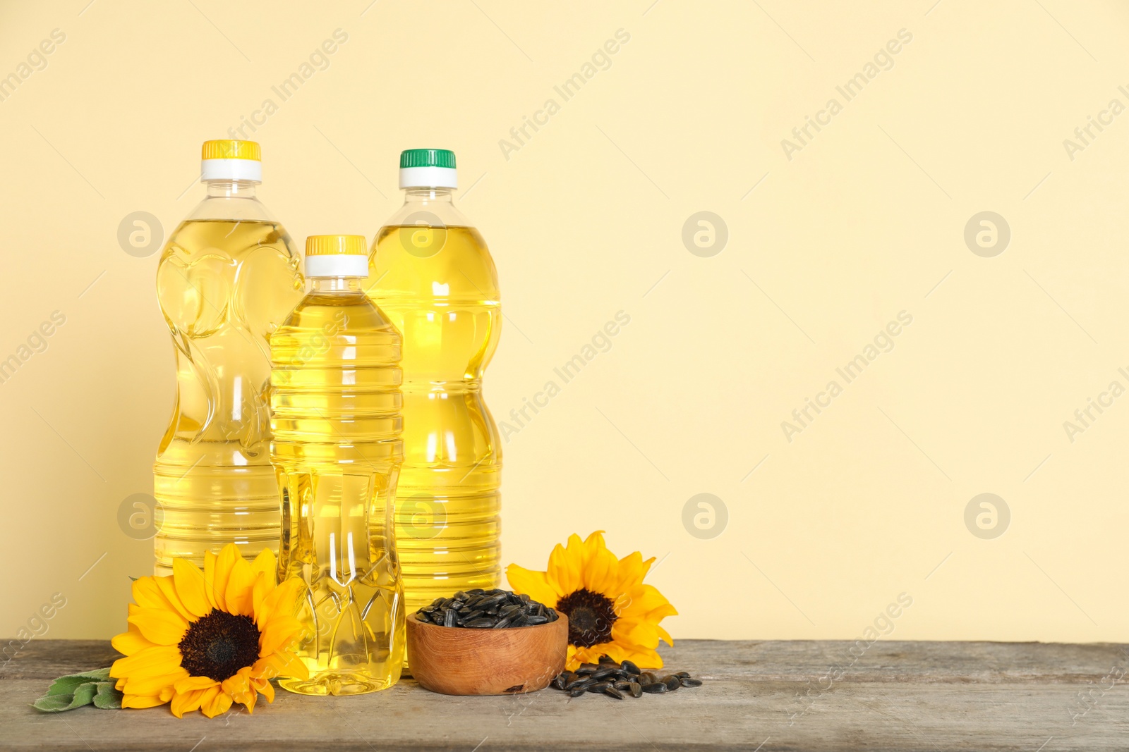 Photo of Bottles of cooking oil, sunflowers and seeds on wooden table, space for text