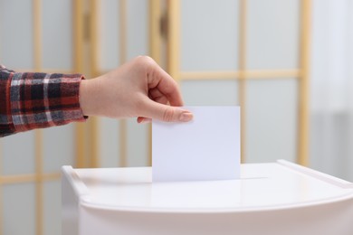 Photo of Woman putting her vote into ballot box on blurred background, closeup