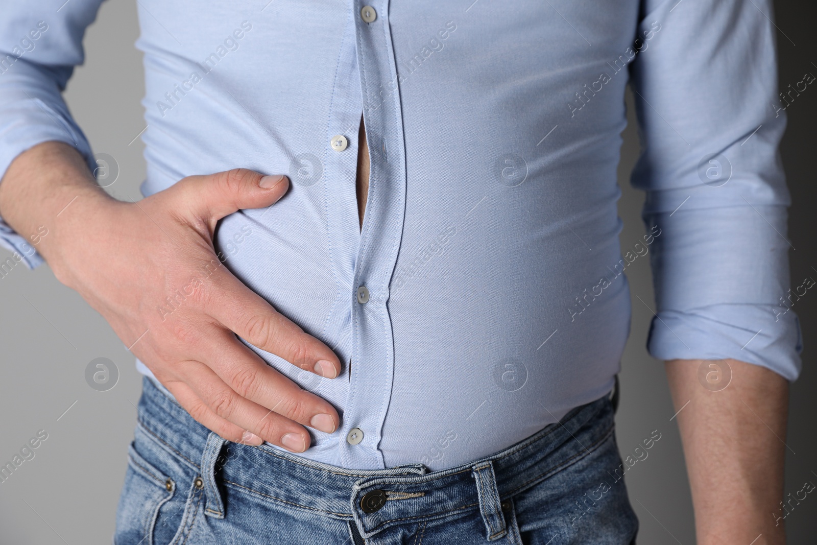 Photo of Overweight man in tight shirt on grey background, closeup