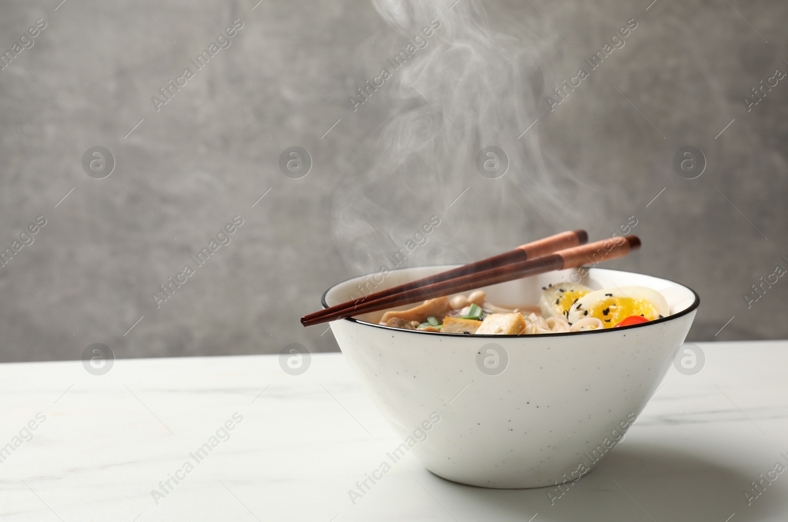 Image of Bowl of hot ramen and chopsticks on white marble table, space for text. Noodle soup