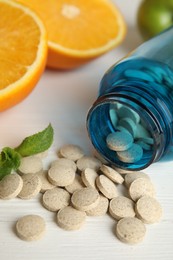 Bottle with vitamin pills and orange on white wooden table, closeup