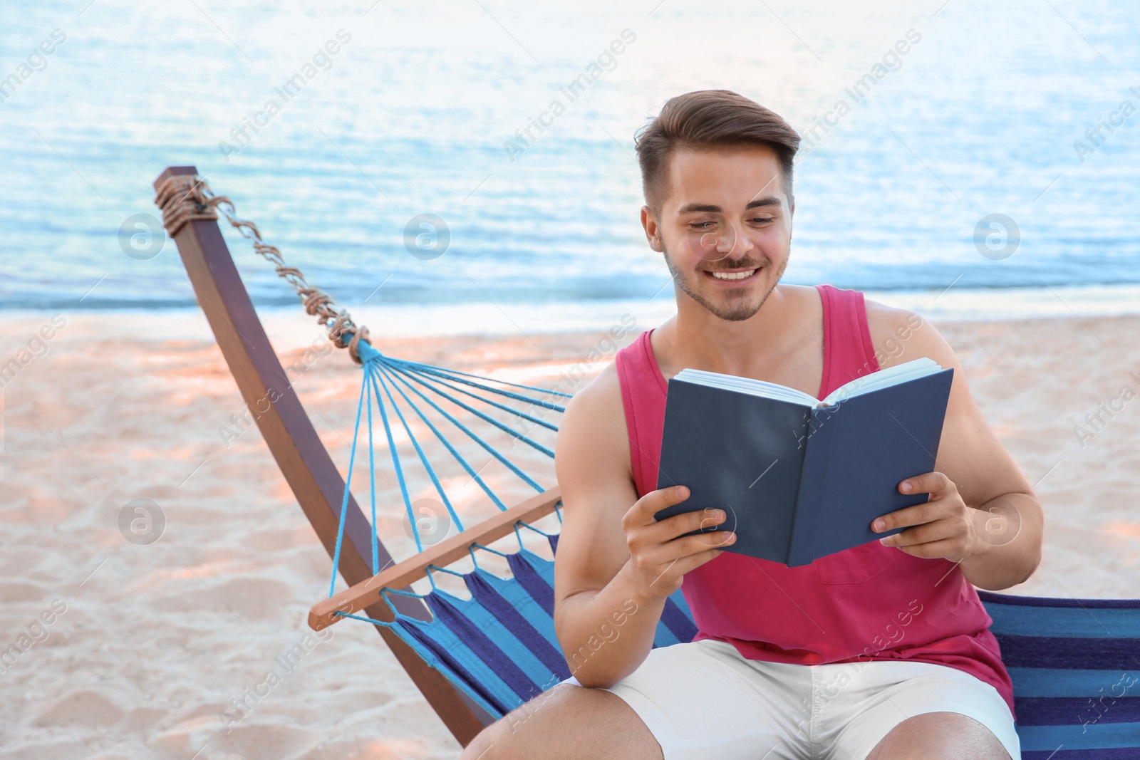 Photo of Young man reading book in hammock at seaside