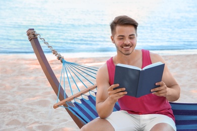 Young man reading book in hammock at seaside