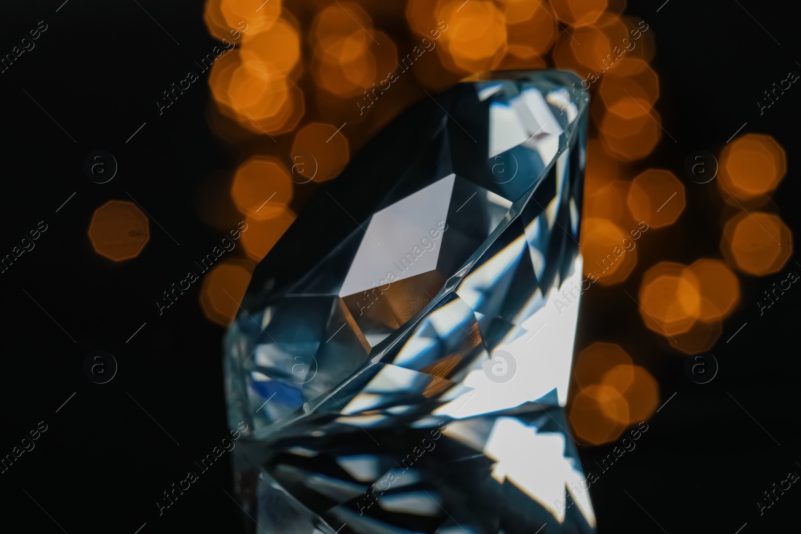 Photo of Large dazzling brilliant on black glass surface against blurred festive lights