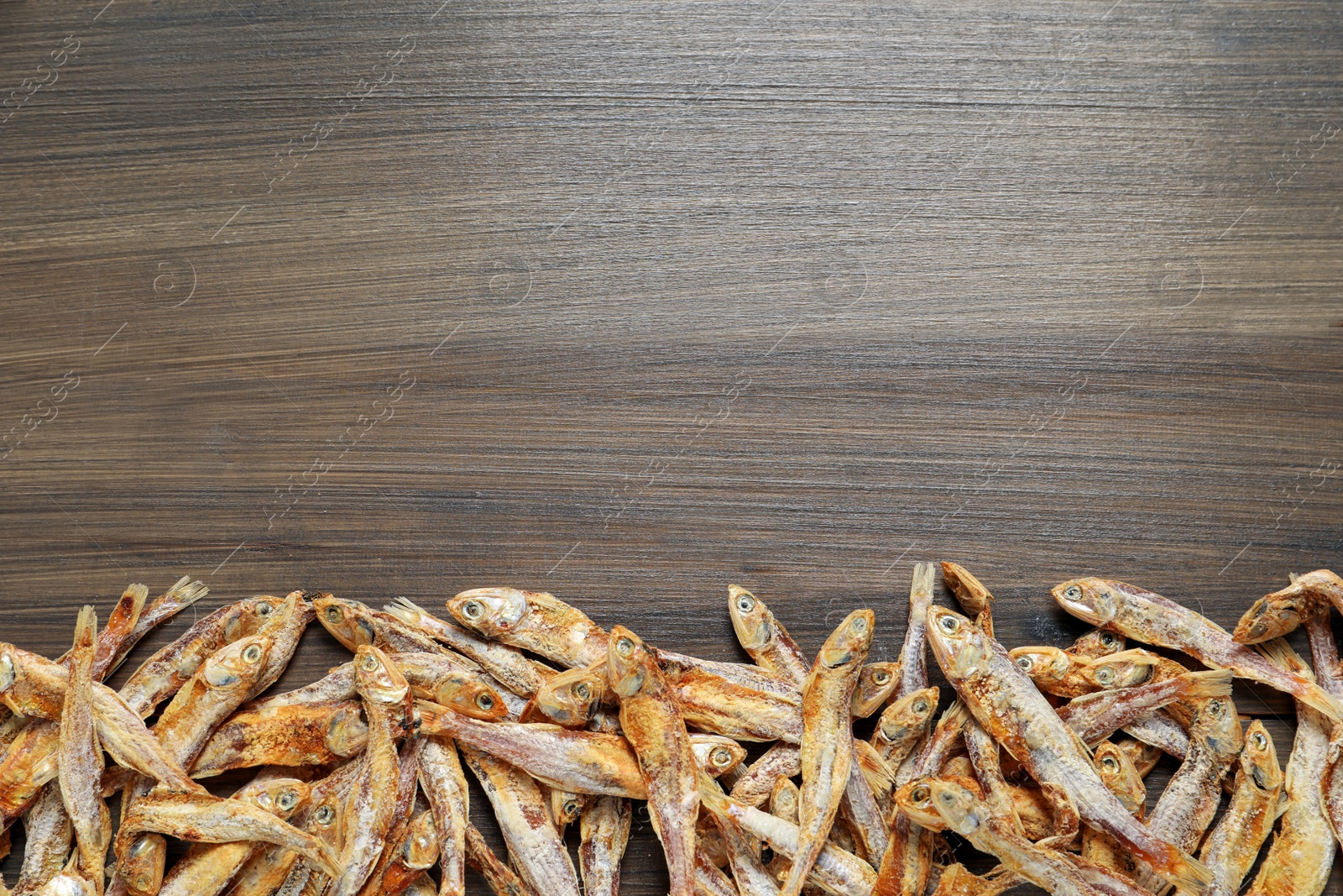 Photo of Tasty dried anchovies on wooden table, flat lay. Space for text