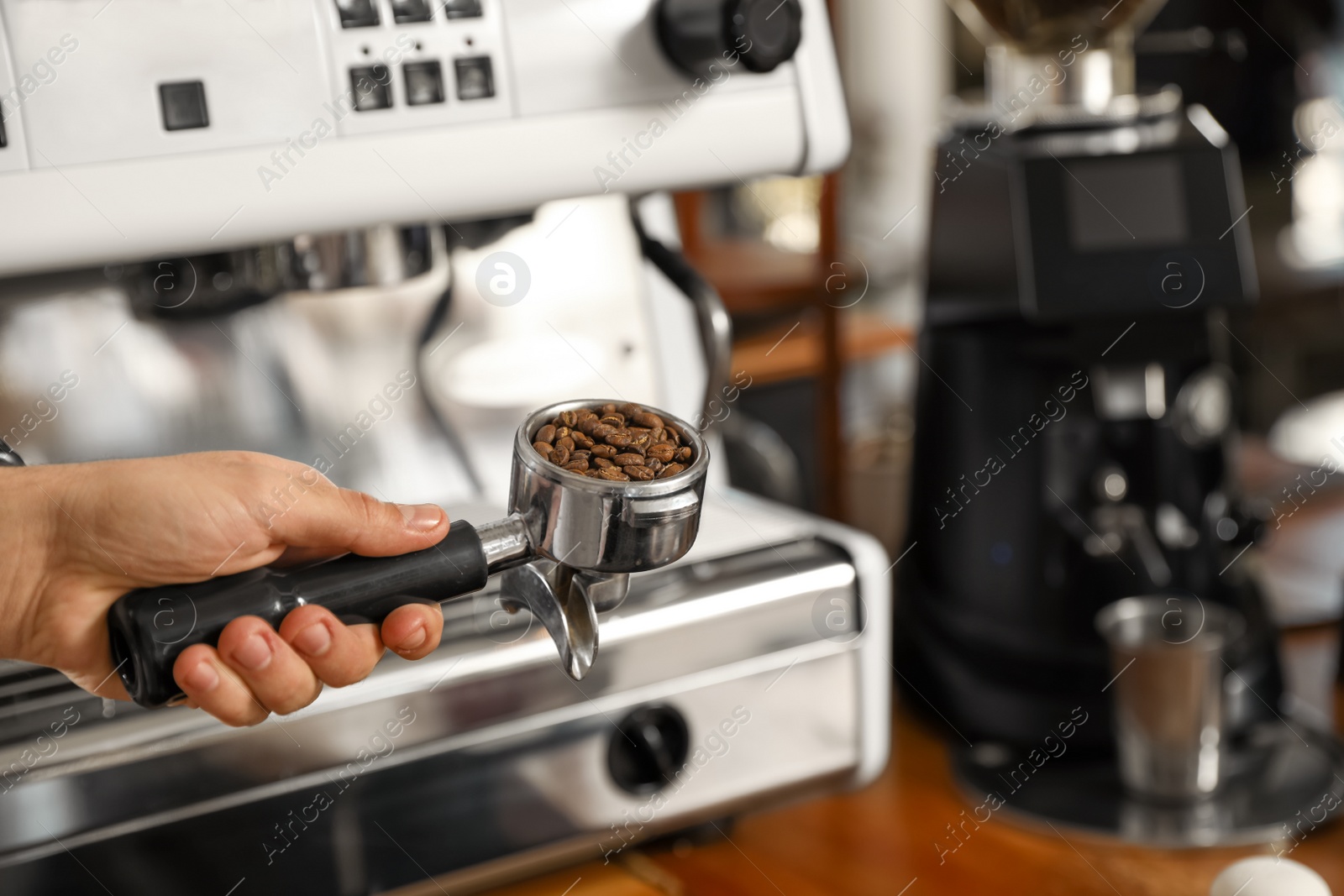 Photo of Barista holding portafilter with coffee beans near machine, closeup. Space for text