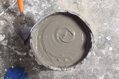 Photo of Bucket of concrete, trowel and gloves on floor indoors, flat lay