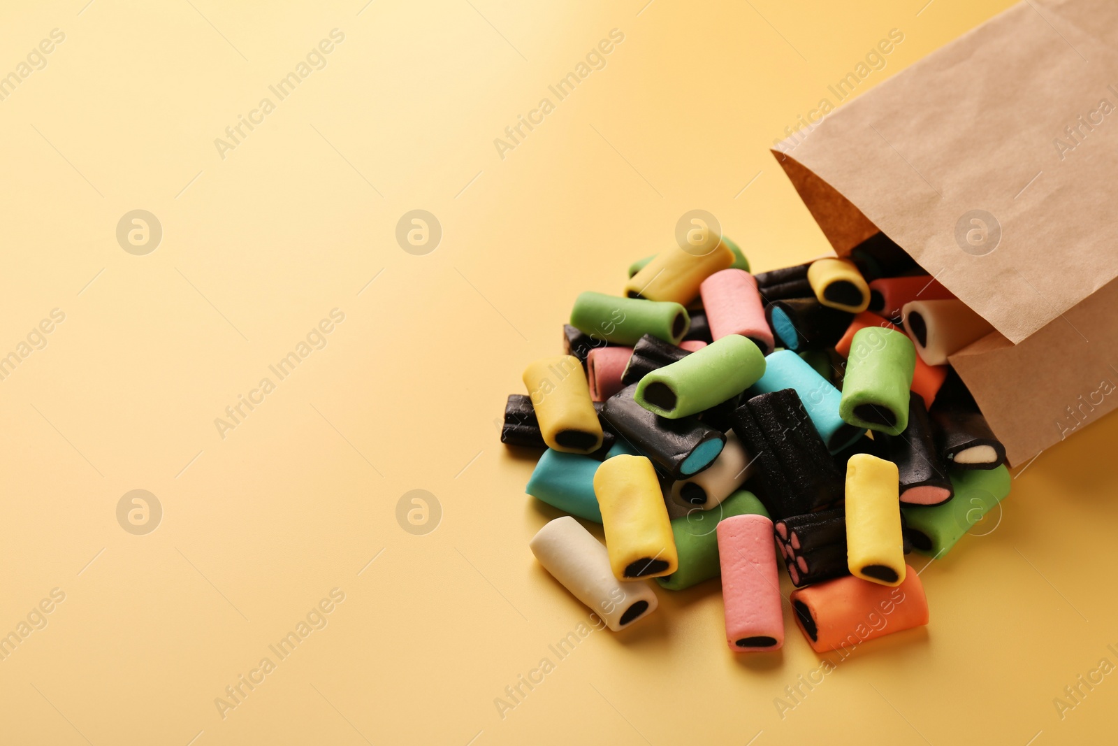 Photo of Tasty liquorice candies and paper bag on yellow background. Space for text