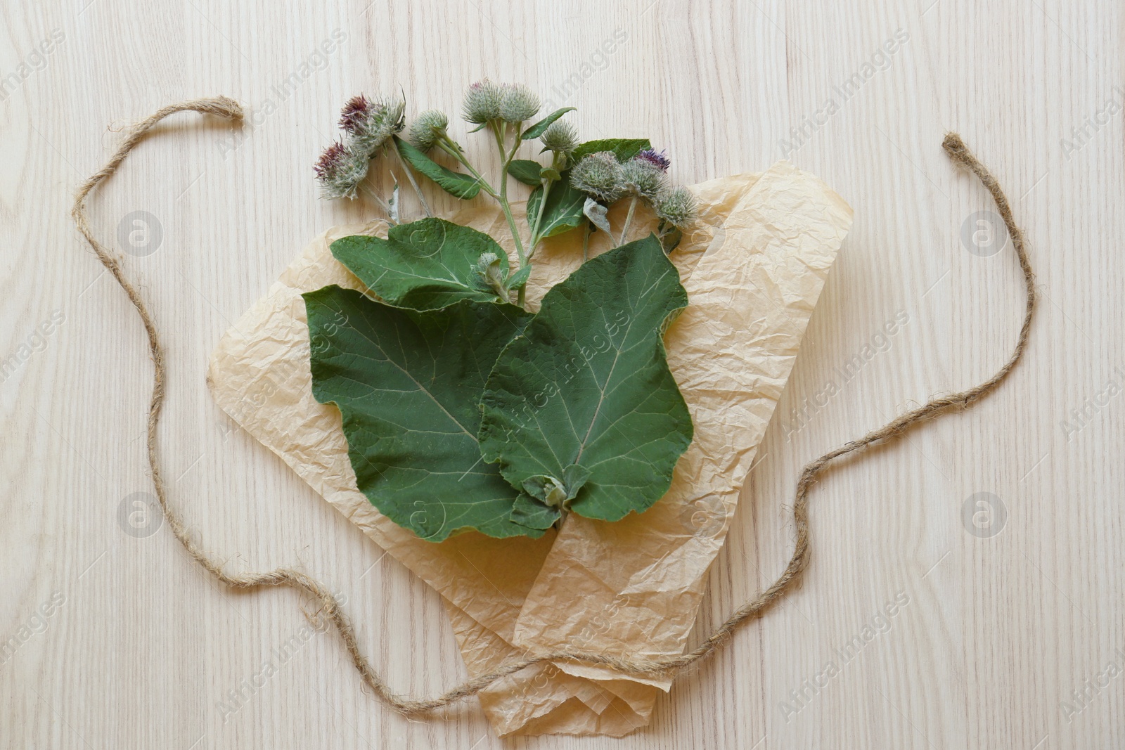 Photo of Fresh green burdock leaves, flowers and wrap paper on wooden table, flat lay