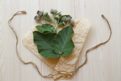 Photo of Fresh green burdock leaves, flowers and wrap paper on wooden table, flat lay