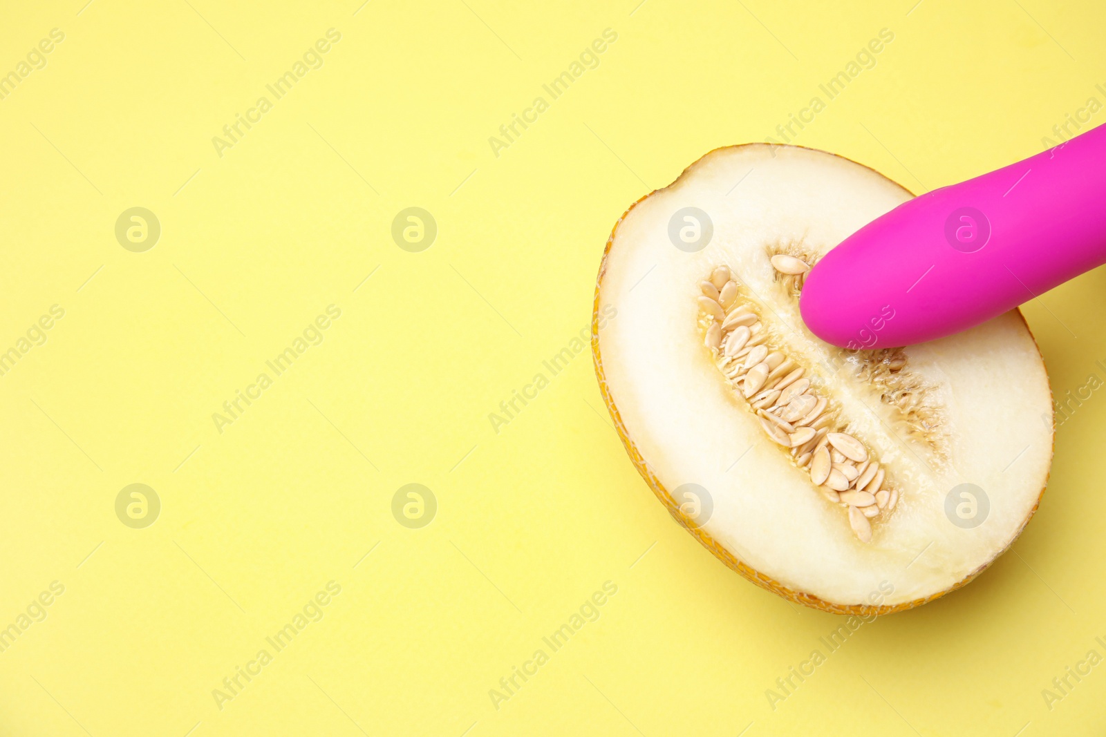 Photo of Half of melon and purple vibrator on yellow background, flat lay with space for text. Sex concept