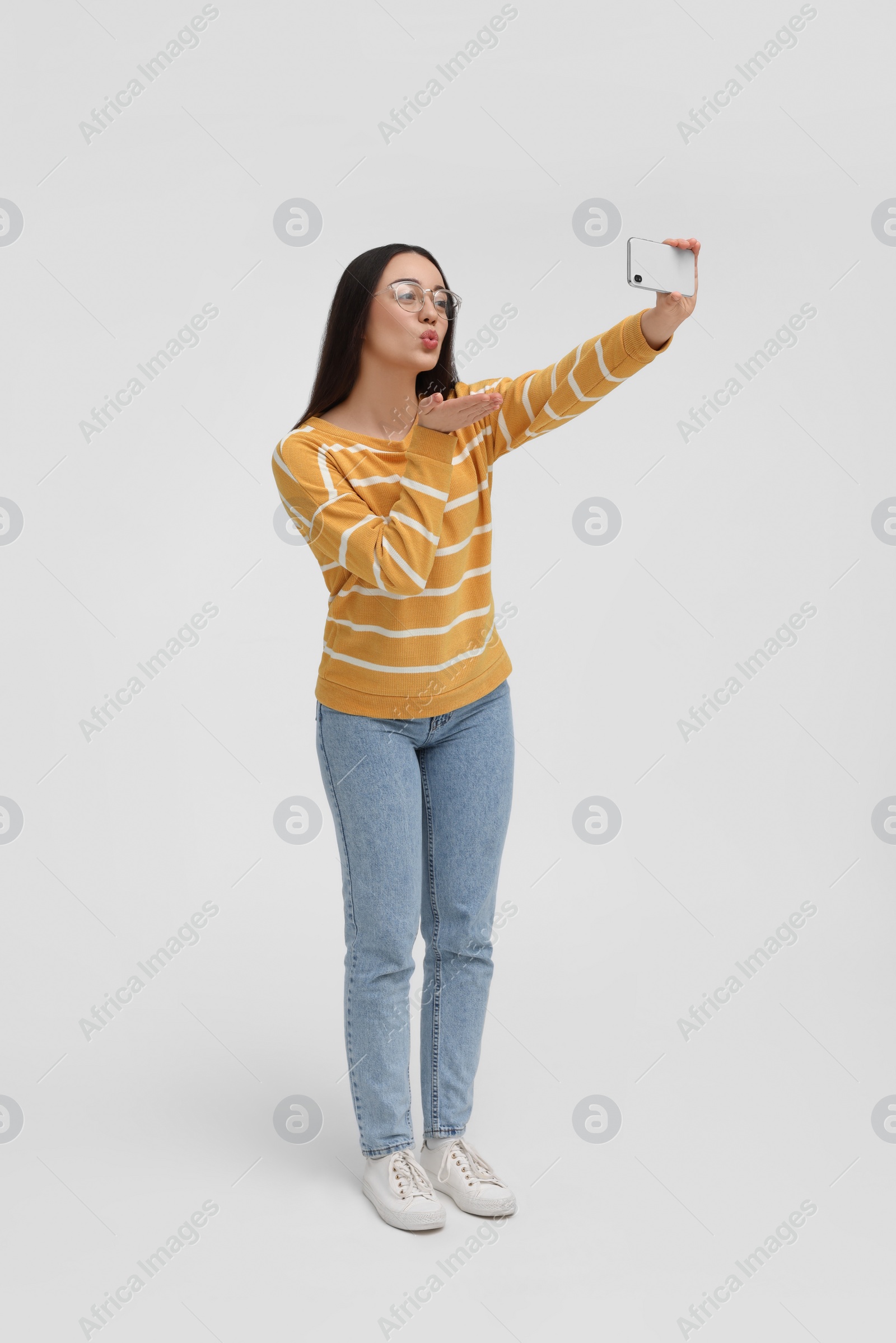 Photo of Young woman taking selfie with smartphone and blowing kiss on white background