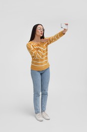 Photo of Young woman taking selfie with smartphone and blowing kiss on white background