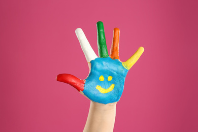 Kid with smiling face drawn on palm against pink background, closeup