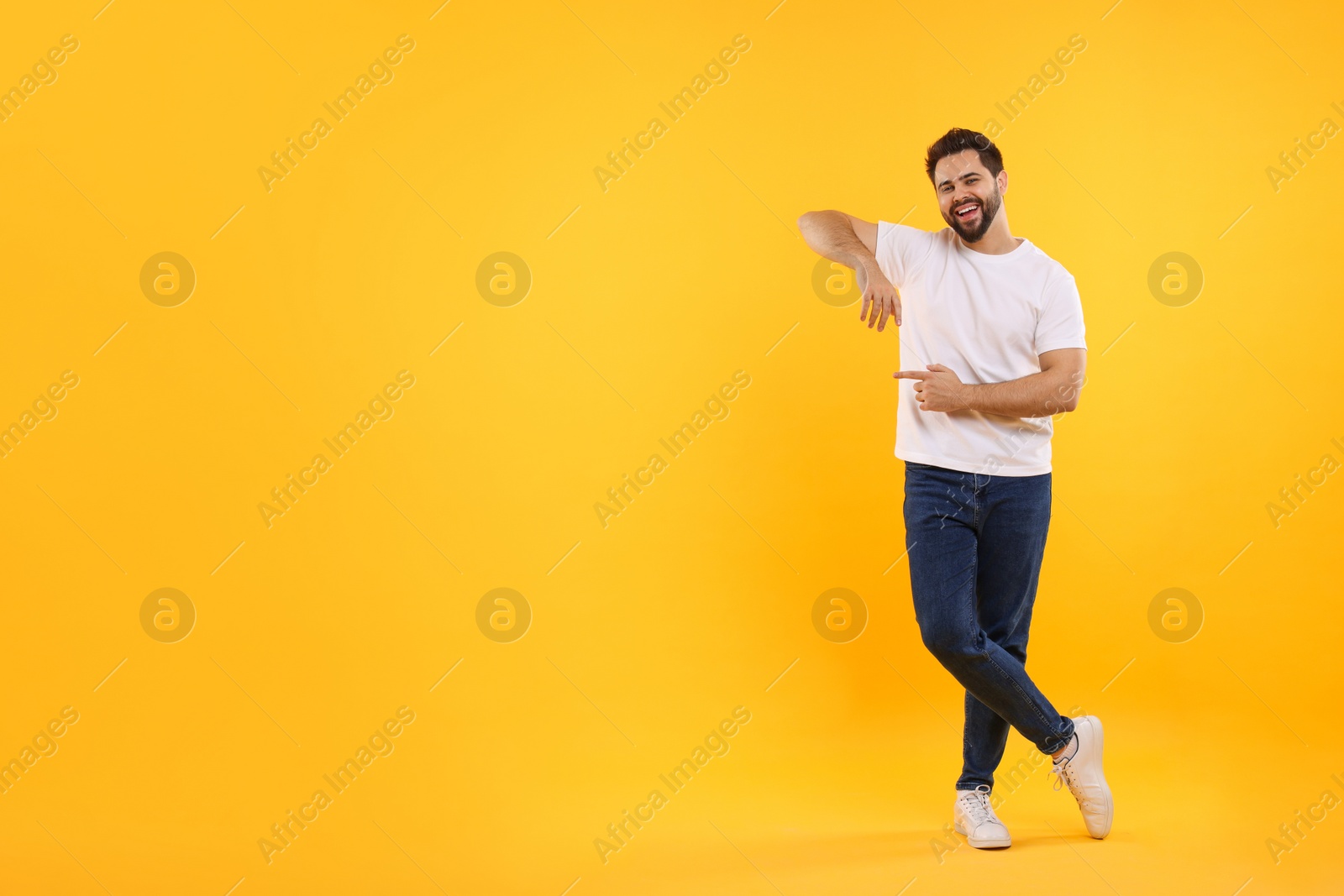 Photo of Happy young man pointing at something on yellow background, space for text