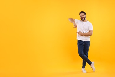 Happy young man pointing at something on yellow background, space for text