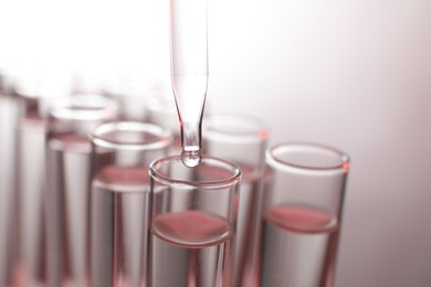 Dripping liquid from pipette into test tube on light background, closeup