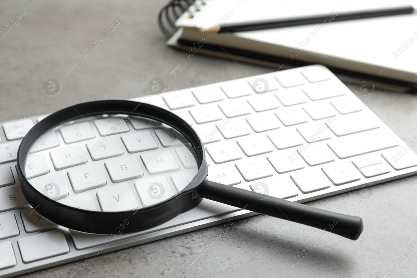 Photo of Magnifier glass and keyboard on light grey stone background, closeup. Find keywords concept