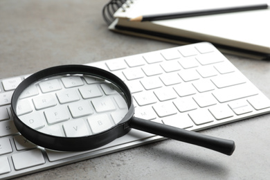 Magnifier glass and keyboard on light grey stone background, closeup. Find keywords concept
