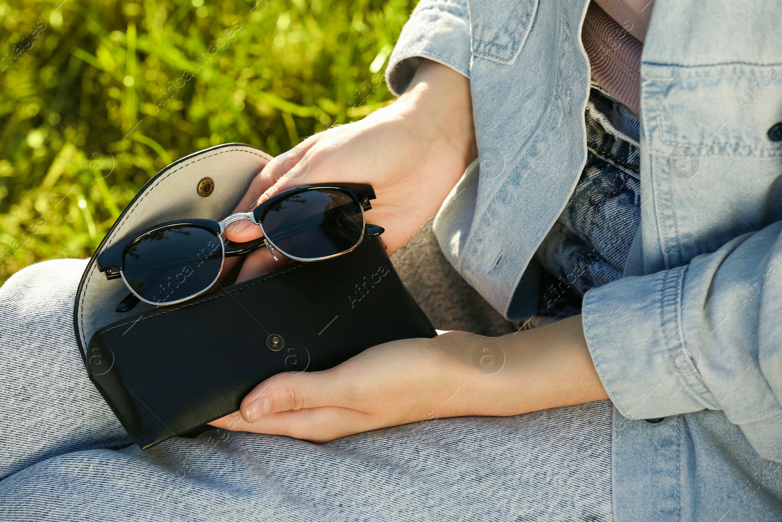 Photo of Woman holding sunglasses and case outdoors on sunny day, closeup