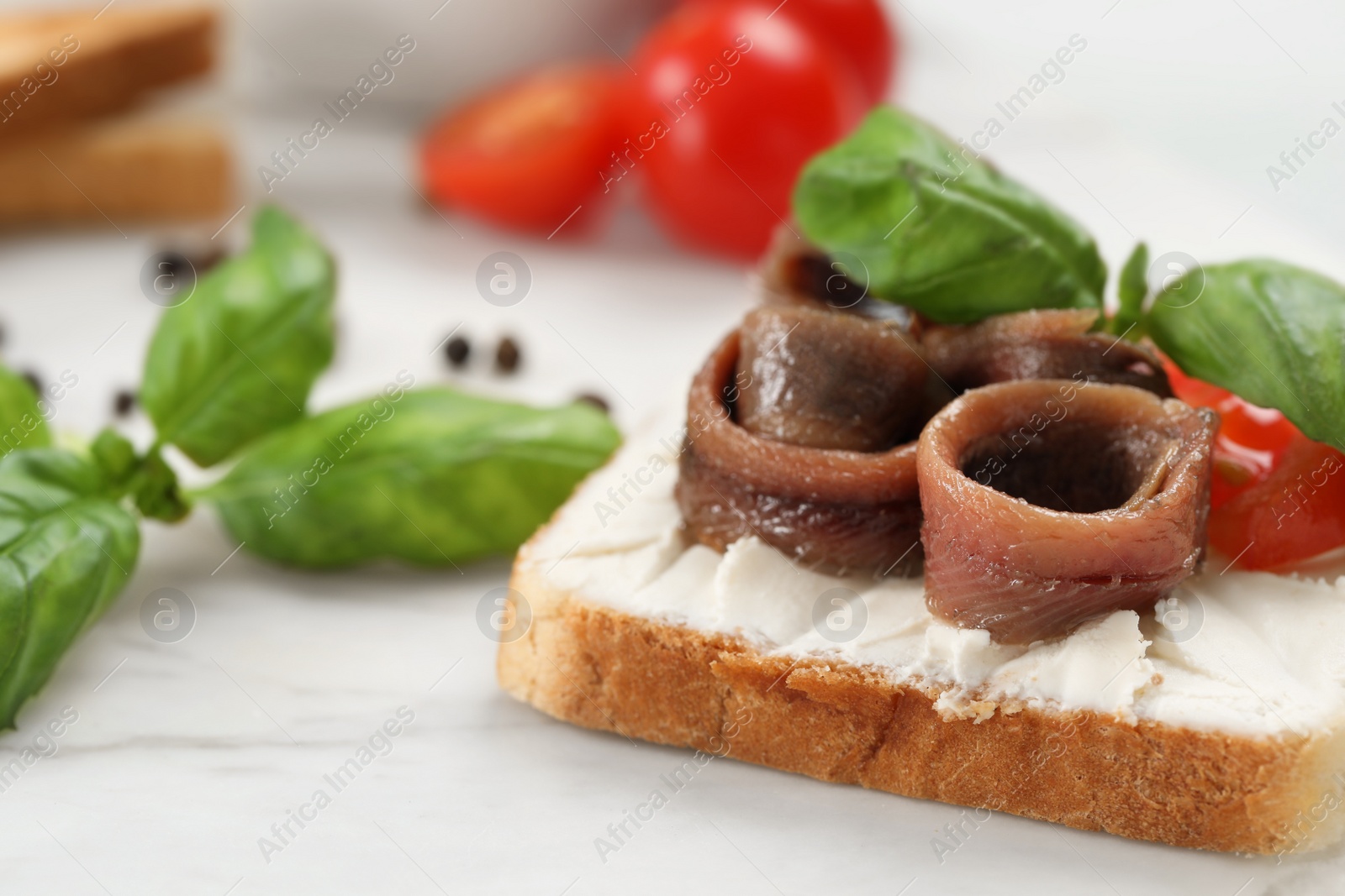 Photo of Delicious sandwich with cream cheese, anchovies and tomato on white marble table, closeup. Space for text