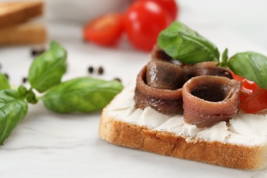 Photo of Delicious sandwich with cream cheese, anchovies and tomato on white marble table, closeup. Space for text