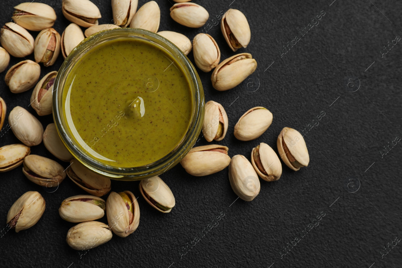 Photo of Delicious pistachio butter and nuts on black table, flat lay